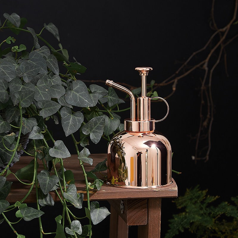 Rose gold atomizer bottle on a wooden surface with green plants in the background