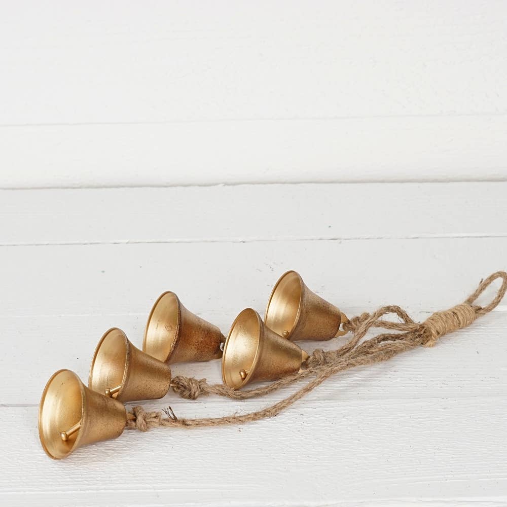 A set of five small metallic gold bells hanging from a natural jute twine string, displayed on a white wooden background.