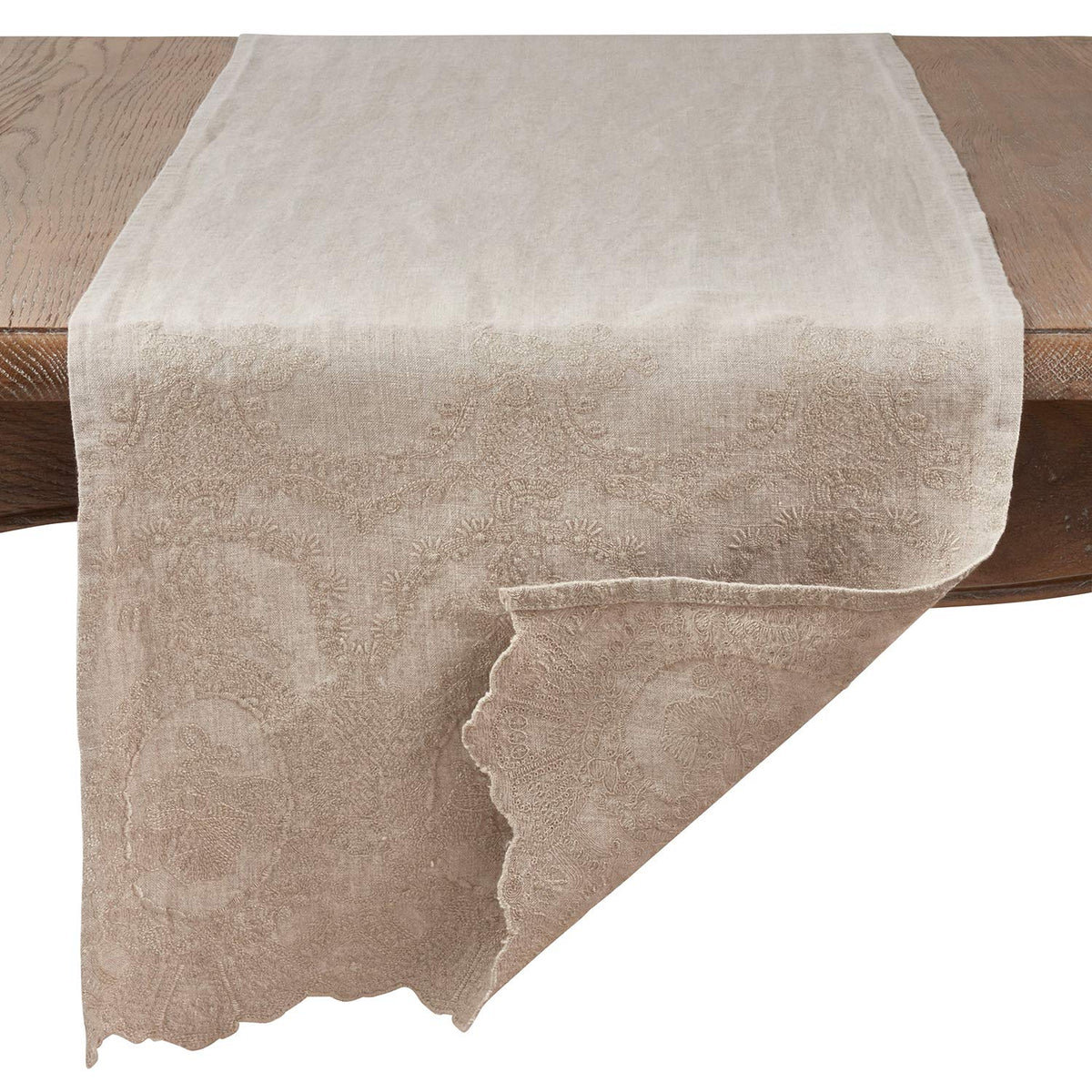 A beige table runner with a subtle damask pattern draped over a wooden table against a white background.