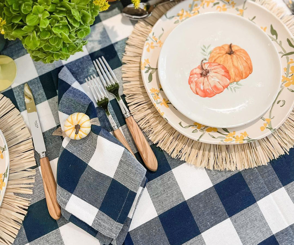 Table setting with a plate featuring pumpkins, cutlery, and a checkered tablecloth.