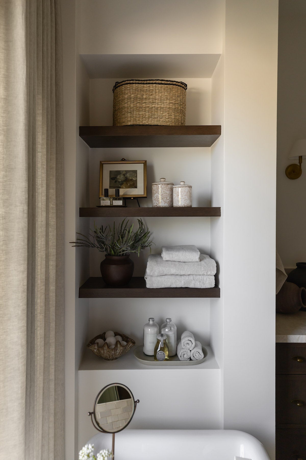 Bathroom shelves with towels, plants, and decorative items against a white wall.