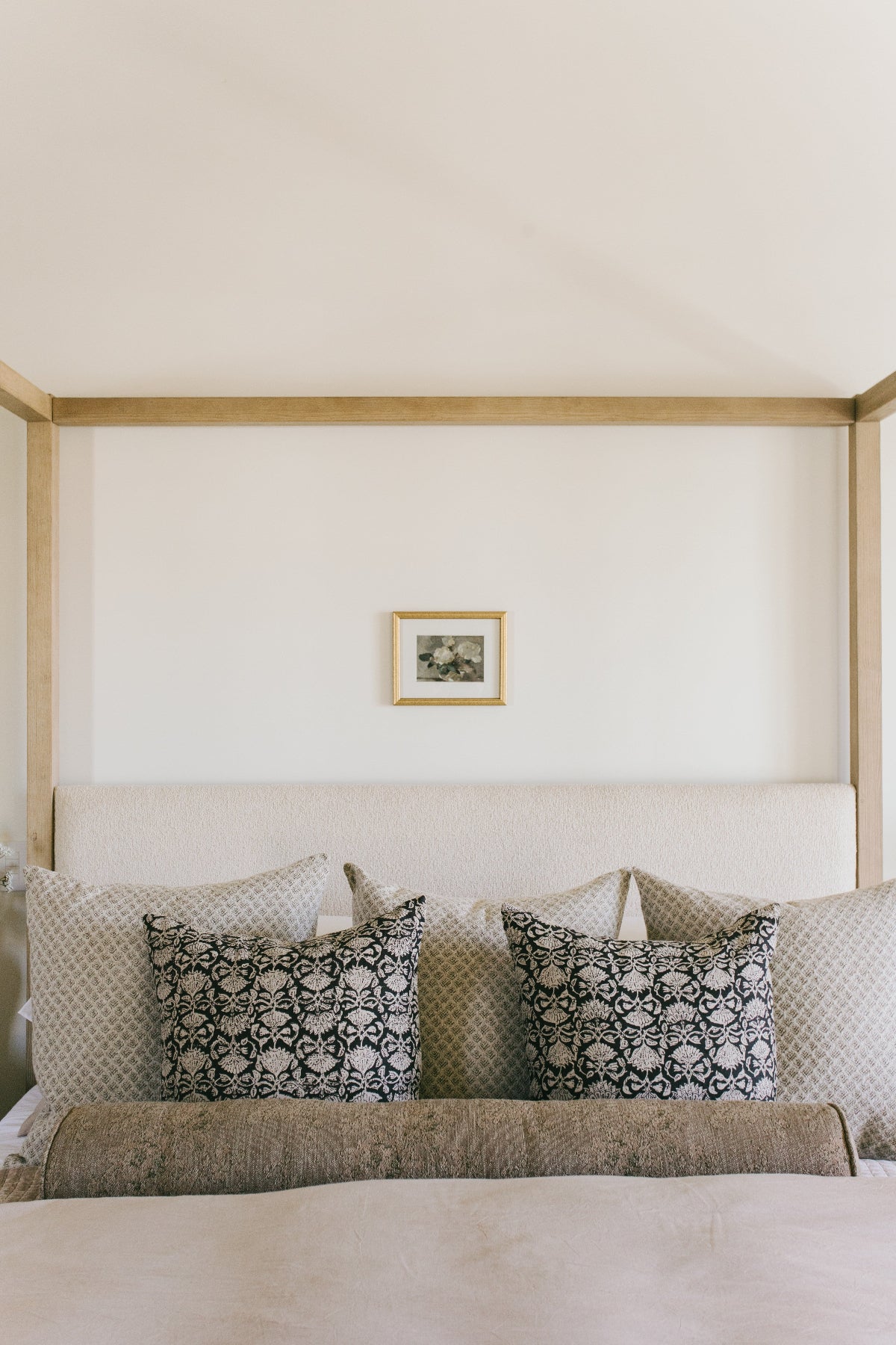 Bed with patterned pillows and a wooden headboard against a white wall.