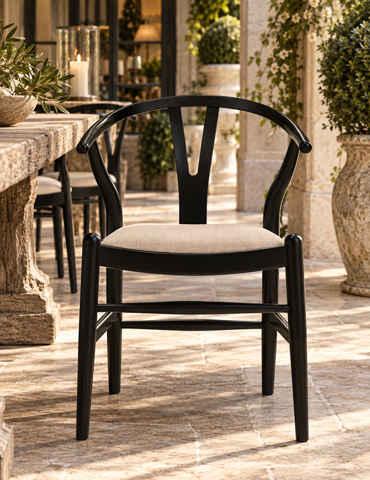 A black wooden dining chair with a curved backrest and a light beige upholstered seat, positioned on a stone patio in an outdoor dining setting.