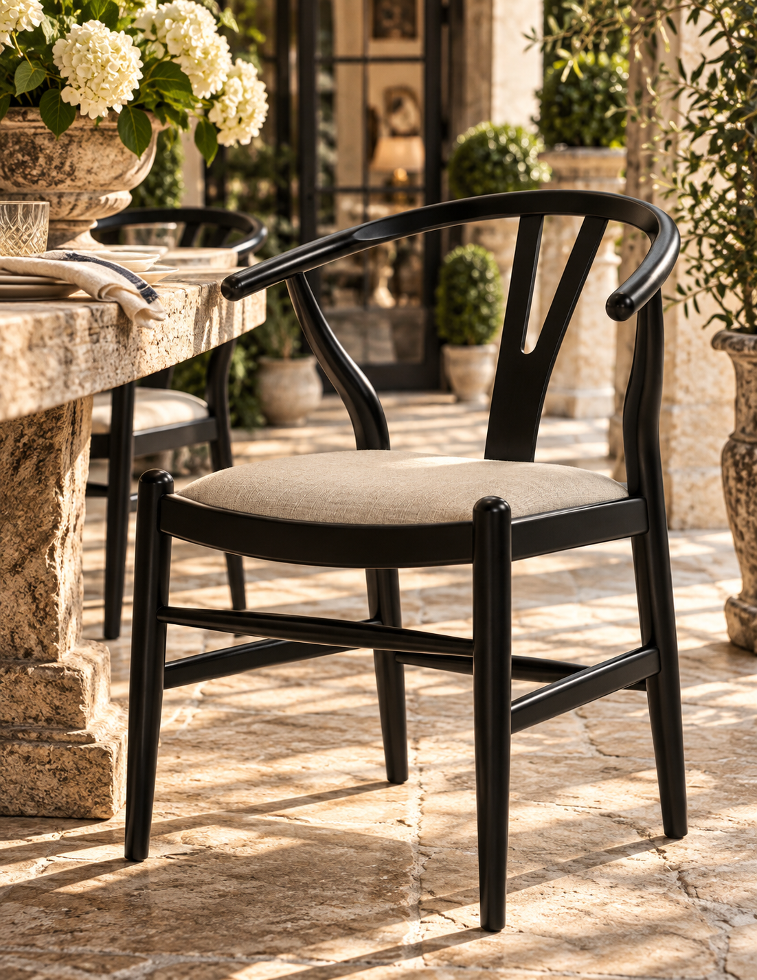 A black wooden dining chair with a curved backrest and a light beige upholstered seat, shown on a stone patio in an outdoor patio setting.