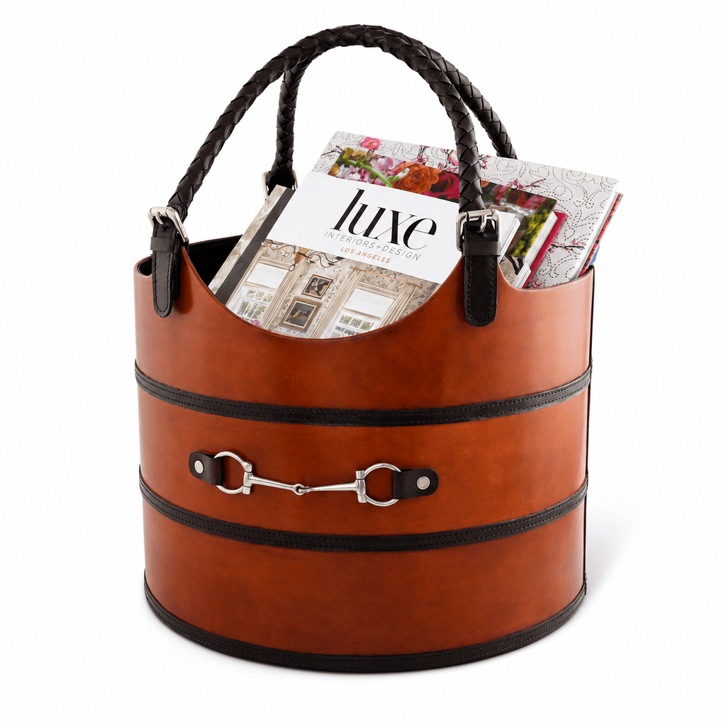 A brown faux-leather cylindrical tote bag with braided top handles, black trim bands, and a silver horsebit detail on the front. Magazines are tucked inside the bag, which is photographed on a clean white background.