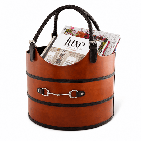 A brown faux-leather cylindrical tote bag with braided top handles, black trim bands, and a silver horsebit detail on the front. Magazines are tucked inside the bag, which is photographed on a clean white background.
