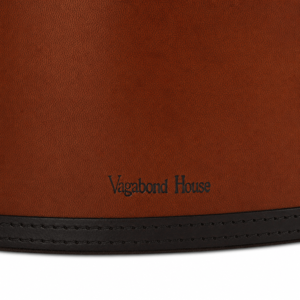 Close-up of a brown leather product with the brand name 'Vagabond House' embossed near the bottom and a black stitched leather trim along the edge, set against a white background.