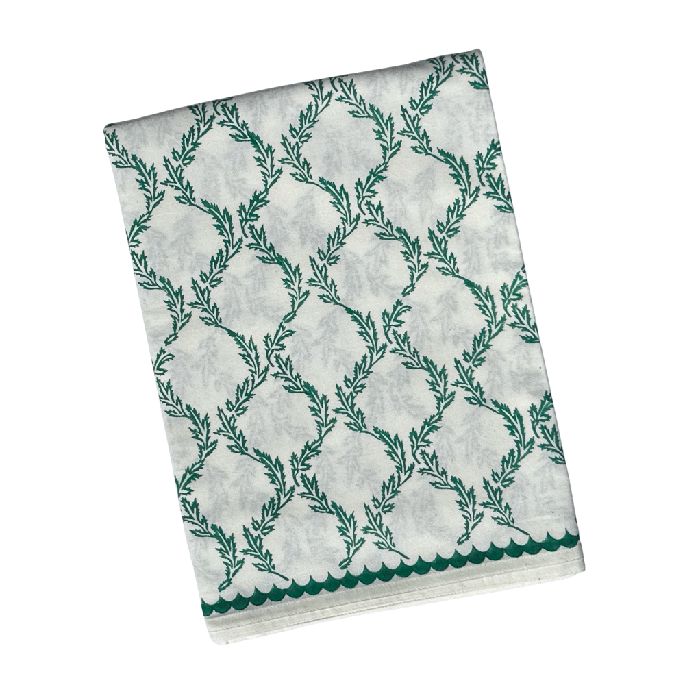 A folded white fabric, likely a saree or scarf, featuring a green trellis pattern made of leafy vines and a scalloped green border along the bottom edge, shown against a plain white background.