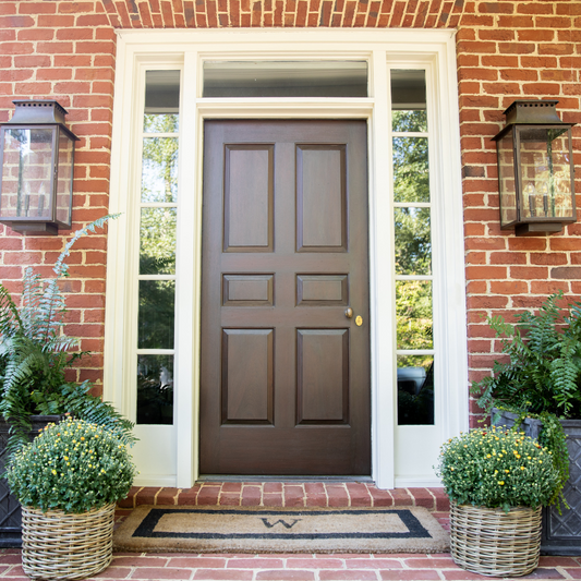 Brown door with glass panels on a brick wall with plants and lanterns.