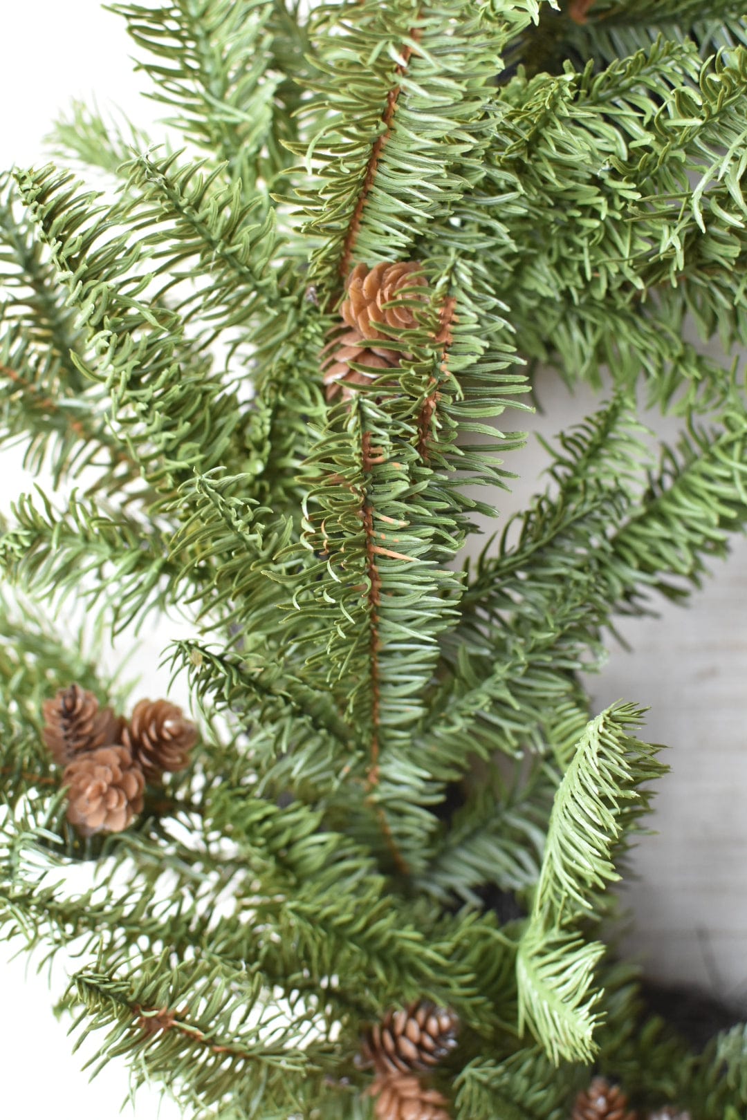 Close-up of green artificial Christmas tree branches with pine cones on a neutral background