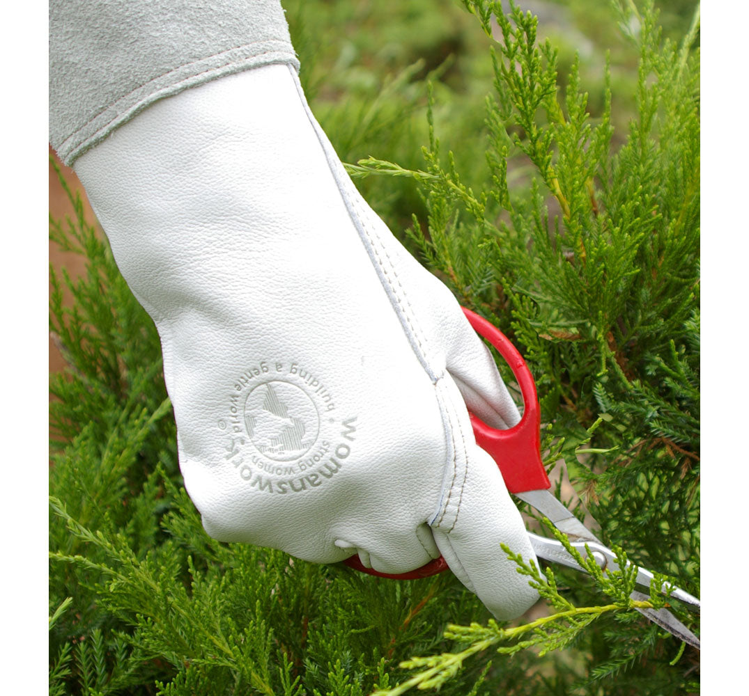 Hand wearing a white gardening glove with a red tool trimming green shrubbery.