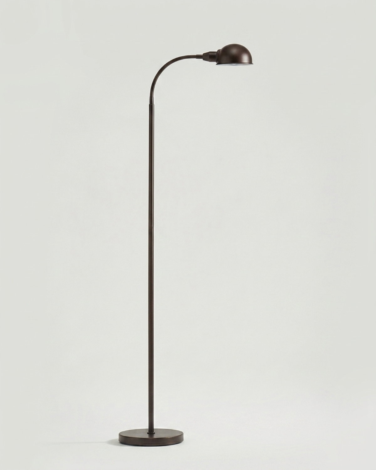 The Regent Apothecary Floor Lamp with an adjustable gooseneck, styled beside a leather Chesterfield sofa in a coastal-inspired home library featuring navy built-in bookcases, antique brass accents, and weathered oak furnishings.