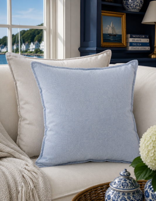 A light blue textured throw pillow with a matching piping border rests on a cream-colored sofa in a beautifully styled living room setting.