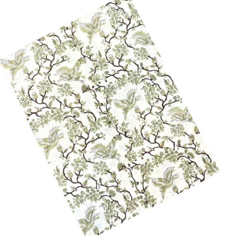A rectangular fabric or paper sheet featuring a classic toile pattern of cranes perched on branches with green leaves on an off-white background, shown diagonally on a white studio background.