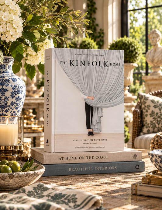 The Kinfolk Home book by Lera Louie Ruttman and Noah Plushen, styled on a table in a beautifully decorated home interior next to a blue and white ceramic vase and green limes.