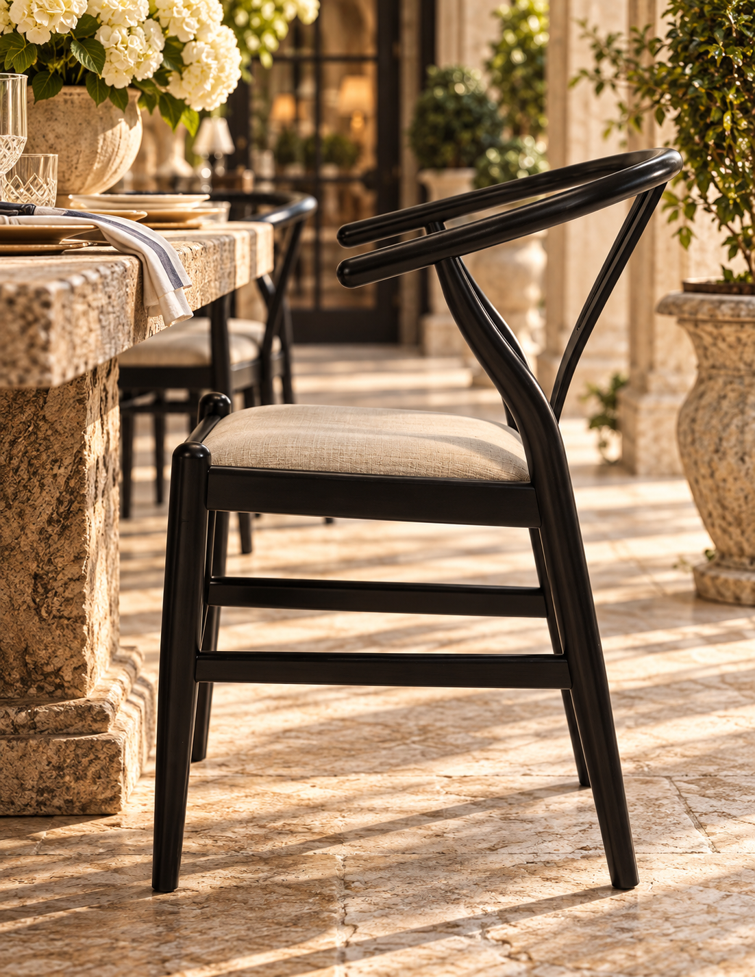 A modern black wooden dining chair with a curved backrest and a light beige upholstered seat, shown in a sunlit outdoor patio setting.
