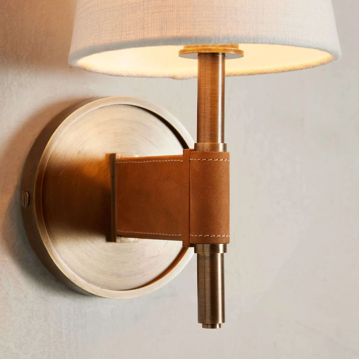 Wall-mounted lamp with brass fixture and leather accent on a neutral background