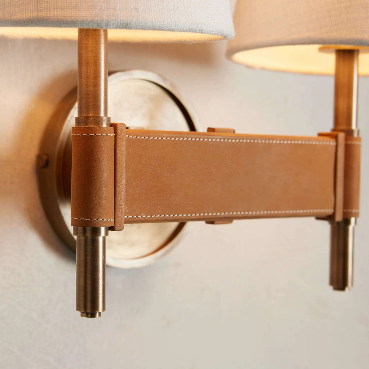 Wall-mounted lamp with leather accent and gold fixtures on a neutral background