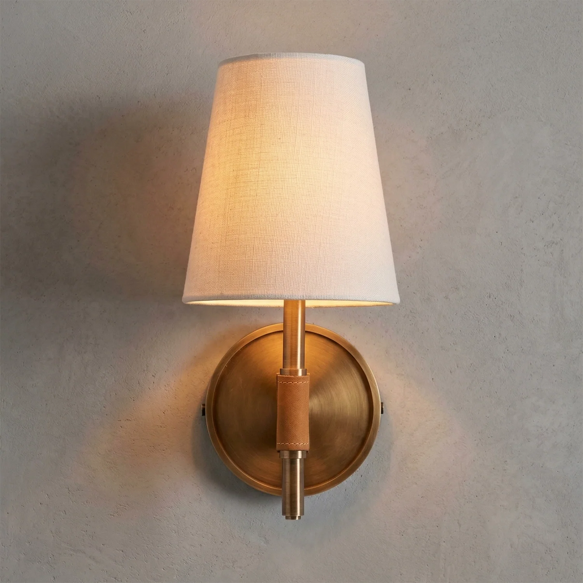 Wall-mounted lamp with a white shade and gold base on a gray wall.