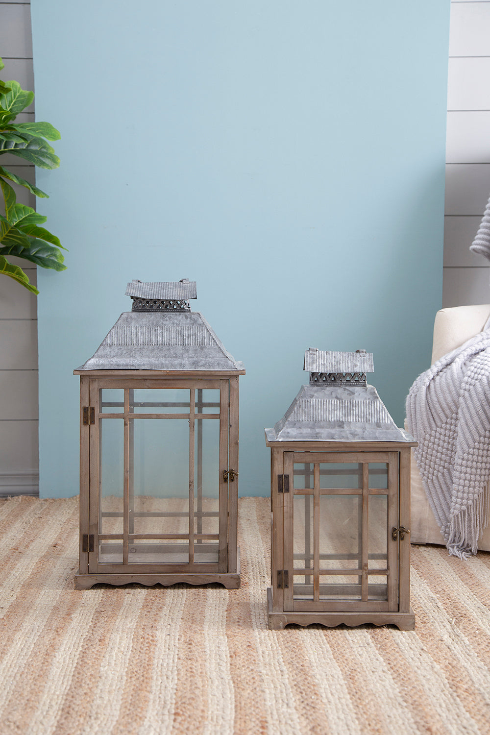 Two rustic wooden lanterns with weathered gray roofs, displayed on a woven jute rug against a light blue wall.