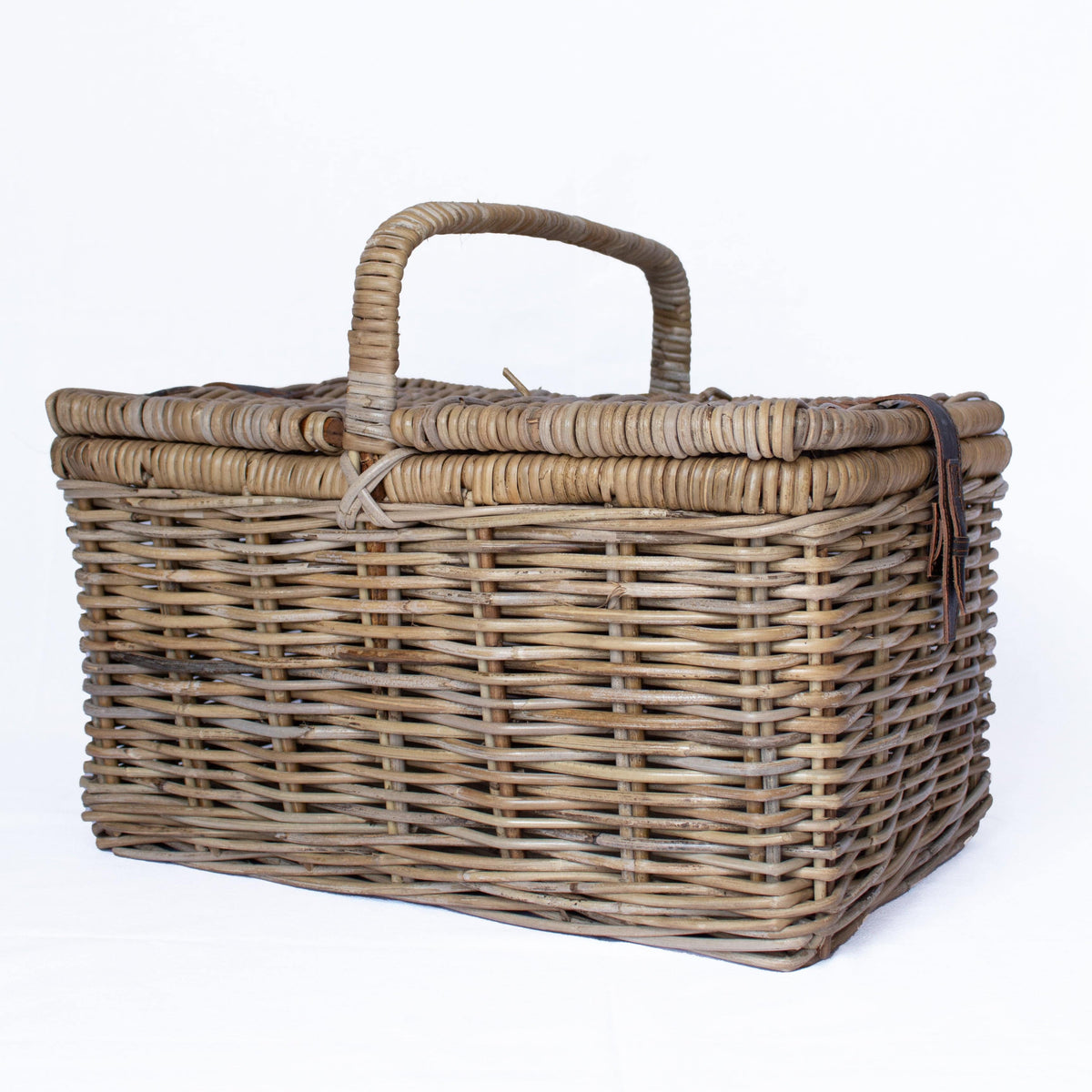 A rectangular woven wicker basket with a lid and a single curved handle, photographed on a clean white background.