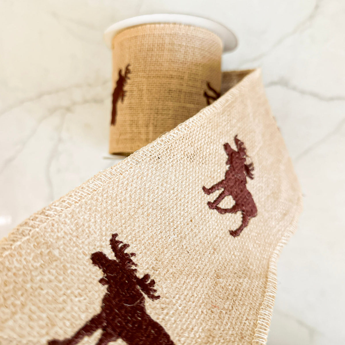 Close-up of beige fabric with brown horse patterns, spool of thread in the background.
