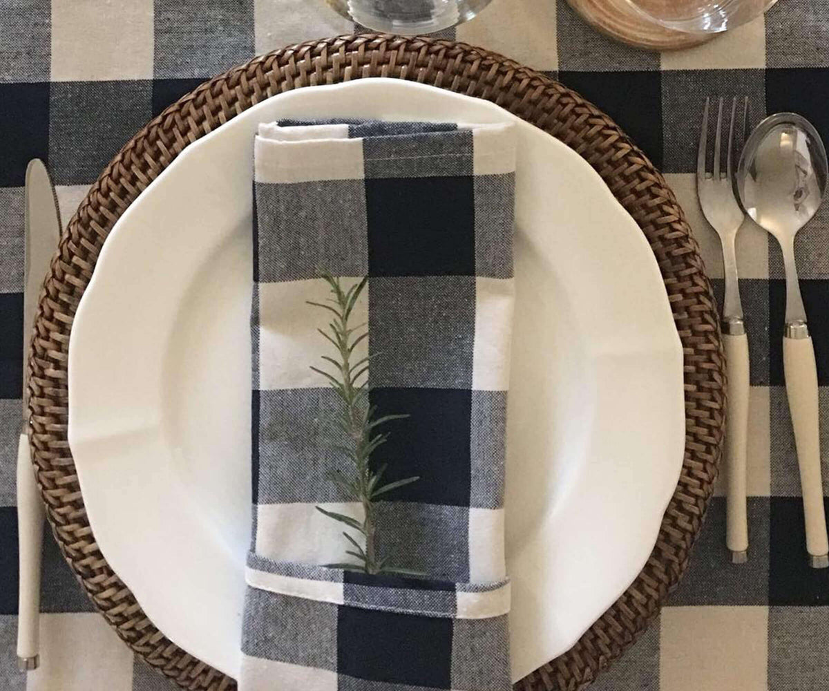 Plaid napkin with a plant design on a white plate with a woven charger, on a checkered tablecloth.