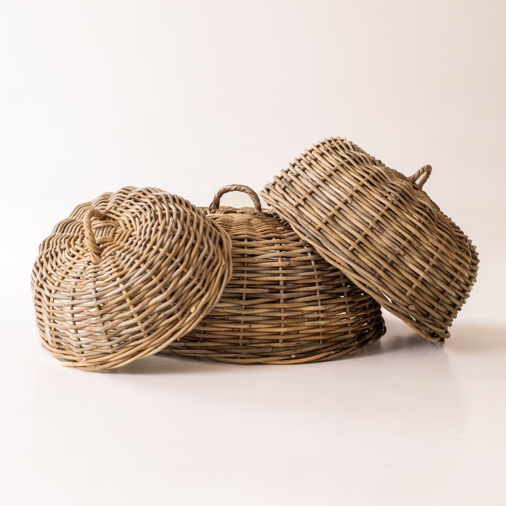 Three woven wicker baskets with matching lids in natural tan and brown tones, arranged on a clean off-white background.