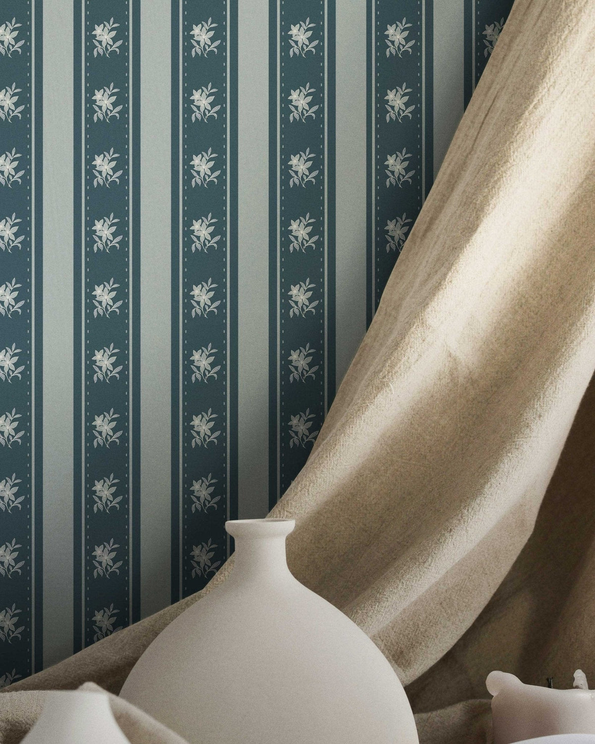 White vase on a surface with striped wallpaper and draped fabric in the background