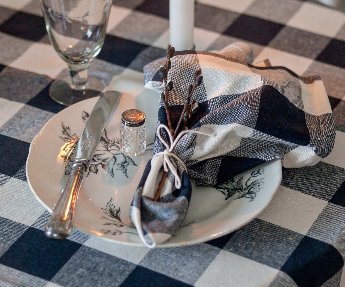 Table setting with a plate, cutlery, and decorative napkin on a checkered tablecloth.