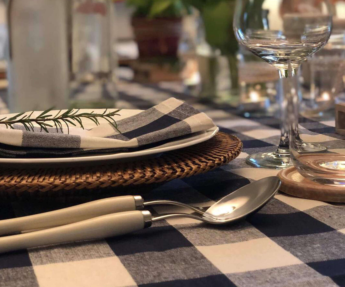 Dining table setting with checkered tablecloth, cutlery, and a folded napkin.
