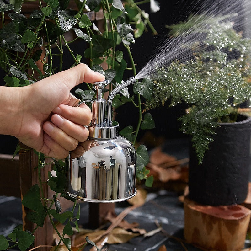 Hand holding a silver watering can over plants